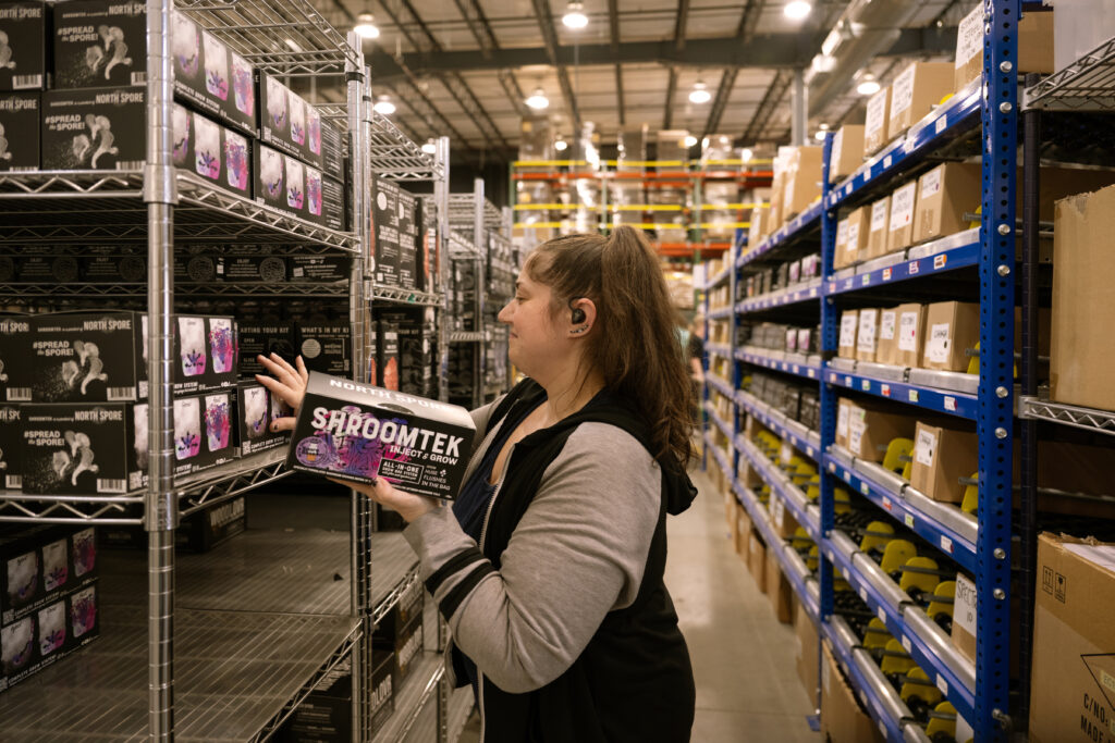 Worker putting final "Shroomtek" grow kit packaging on shelf